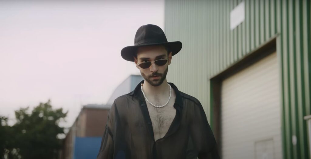 Ein Ausschnitt aus dem Musikvideo "Trigger Mich". Man sieht einen Mann mit Sonnenbrille und Hut.